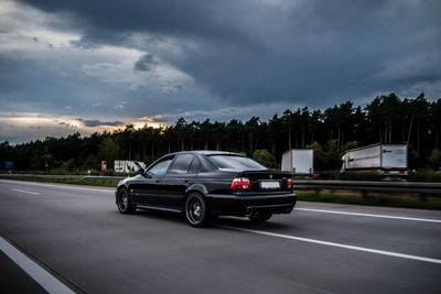 Cars on road against cloudy sky