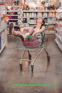 The girl is sitting in a basket in the trading floor. a lady rides in a cart in an empty store