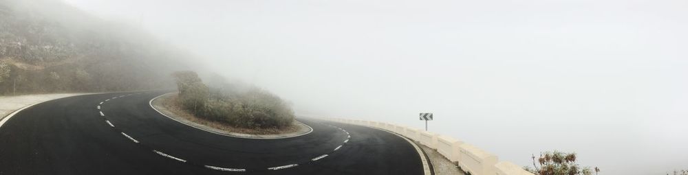 Road by mountains against sky during foggy weather