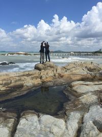 People standing on rock at beach against sky