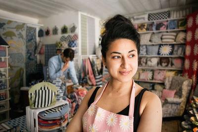 Confident smiling woman looking away while colleague working in shop