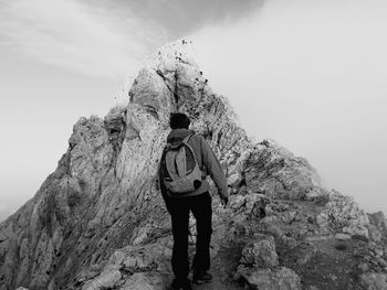 Rear view of man standing on rock formation against sky