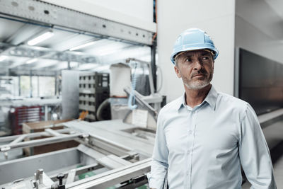 Contemplating male engineer wearing hardhat while looking away in manufacturing industry