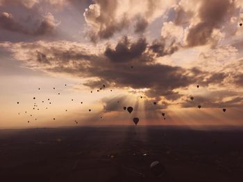 Hot air balloons flying against cloudy sky during sunset