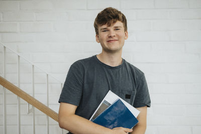 Portrait of smiling male student holding books standing in university