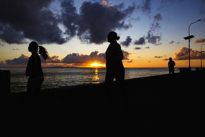 Silhouette people on beach against sky during sunset