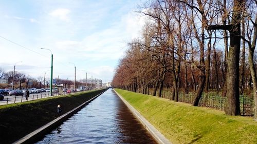 Canal amidst bare trees against sky in city