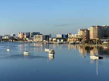 Sailboats moored on river by buildings against clear blue sky