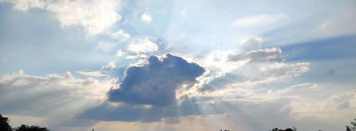 Low angle view of sunlight streaming through clouds