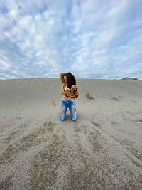 Woman with umbrella on sand dune in desert against sky