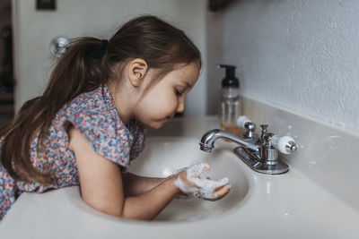 Side view of young girl washing hands in sink with soap