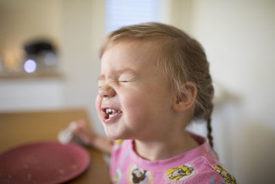 Cute toddler girl making funny faces at the table.