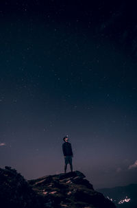 Low angle view of young man standing on cliff against star field