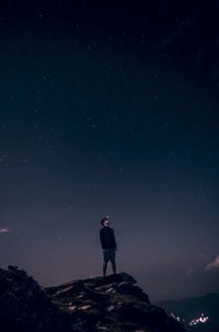 Low angle view of young man standing on cliff against star field