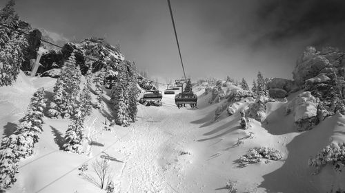 Ski lifts over snow covered field against sky