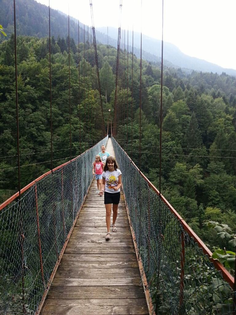 lifestyles, full length, leisure activity, tree, rear view, railing, connection, bridge - man made structure, men, footbridge, walking, the way forward, person, casual clothing, transportation, bridge, forest