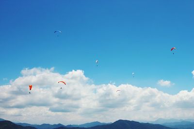 Low angle view of people paragliding against blue sky