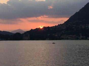 Scenic view of sea by mountains against sky during sunset