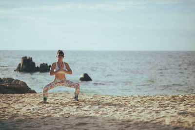 Full length of woman exercising on beach against sky