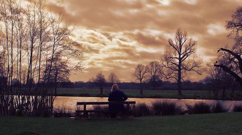 Woman sitting by lake against sky during sunset