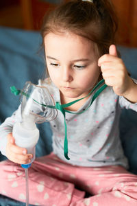Girl holding oxygen mask while sitting on bed