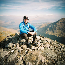 Portrait of smiling young man sitting on rocks by mountains