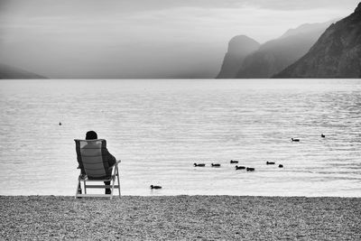 Rear view of man sitting at beach during sunset