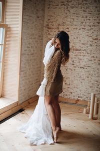 Woman holding wedding dress while standing against wall