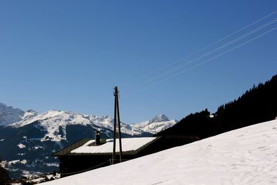 Low angle view of snowcapped mountains against clear blue sky