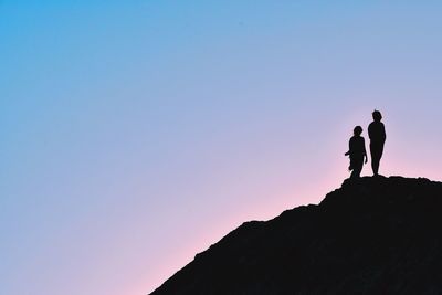 Low angle view of silhouette people standing on rock against clear sky