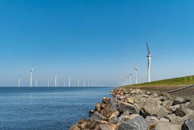 Traditional windmill by sea against clear blue sky, 