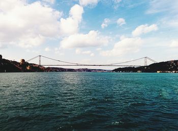 View of suspension bridge over sea against cloudy sky