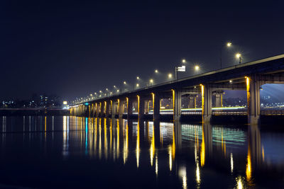 Illuminated bridge over river against sky at night