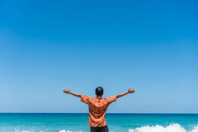 Rear view of man with arms outstretched standing at beach against sky