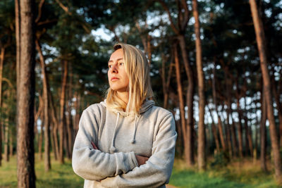 Portrait of a young blond woman walking in a pine forest at dawn.