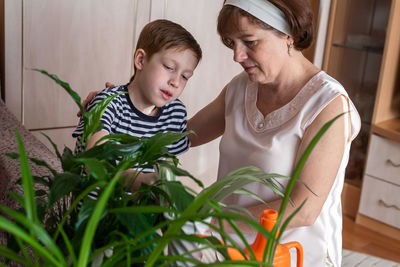 Grandmother and her little grandson red-haired boy 6-7 years old watering flowers together, family