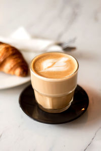 Flat white coffee in a glass cup with croissant 