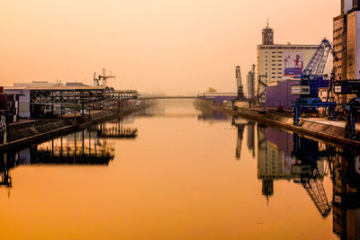 Scenic view of lake by buildings against sky during sunset