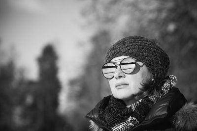 Close-up of woman in warm clothing wearing sunglasses against bare trees