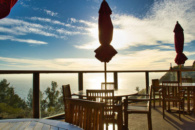 Chairs and tables on table by sea against sky during sunset