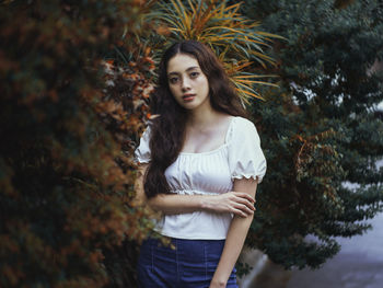 Portrait of beautiful young woman standing against plants