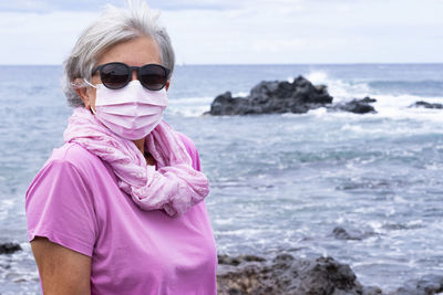 Portrait of senior woman wearing mask standing against sea