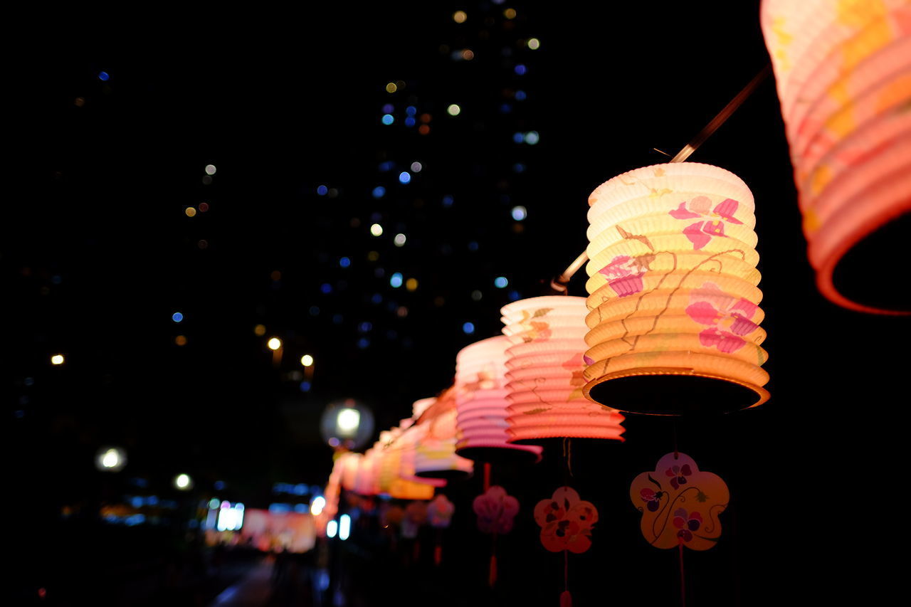 LOW ANGLE VIEW OF ILLUMINATED LANTERNS AGAINST SKY AT NIGHT