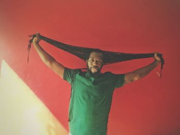 Portrait of man with dreadlocks standing against red wall