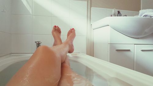 Low section of sensuous woman relaxing in bathtub at bathroom