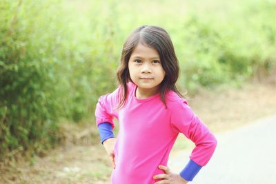 Portrait of cute girl standing on footpath against plants