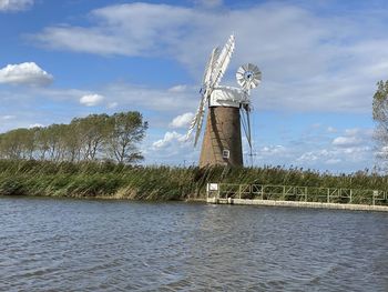 Traditional windmill by lake against sky