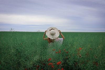 Rear view of woman with white hat and dress standing on a green field and looking into the distance