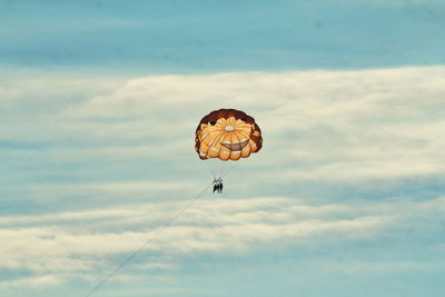 Low angle view of people paragliding against cloudy sky