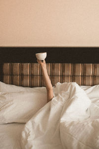 Girl lying in bed holding cup of coffee closeup in hotel room. good sunday morning. breakfast.